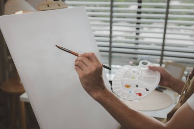 Bir sanatçı kendi resim stüdyosunda tuval, palet, suluboya, yağlar, poster renkleri, sanatsal, ressam, renkler, yaratıcılık, beceri gibi çeşitli resim aletleriyle oturuyor.