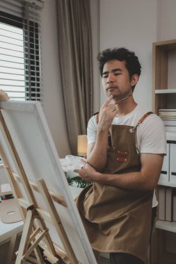 Bir ressam resim stüdyosunda, yükselen bir erkek sanatçı hem resim, palet, tuval, boya, yağlı boya boya, poster renkleri gibi en iyi tablolarını yapmaya odaklanıyor..