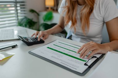 Bir iş kadını ofiste hesap makinesi kullanıyor, şirket bakiyesini kağıt işlerinden kontrol ediyor, finans bilgilerini hesaplıyor, istatistik pazarlama raporlarını hesaplıyor