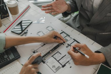 Mühendisler oturmuş yapıyı güçlendirmek için gözden geçirilmesi gereken bir inşaat planını tartışıyorlar. Bir mimar ve asistan planları inceliyor ve inceliyor.