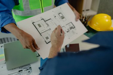 Bir mühendis asistanıyla birlikte ofiste. Plandaki her detayı inceliyorlar. İki mimar büyük proje hakkında fikir alışverişinde bulunuyorlar.