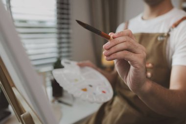 Bir sanatçı kendi resim stüdyosunda tuval, palet, suluboya, yağlar, poster renkleri, sanatsal, ressam, renkler, yaratıcılık, beceri gibi çeşitli resim aletleriyle oturuyor.
