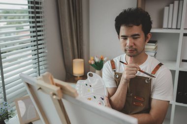 Bir ressam resim stüdyosunda, yükselen bir erkek sanatçı hem resim, palet, tuval, boya, yağlı boya boya, poster renkleri gibi en iyi tablolarını yapmaya odaklanıyor..