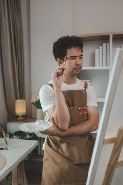 Bir ressam resim stüdyosunda, yükselen bir erkek sanatçı hem resim, palet, tuval, boya, yağlı boya boya, poster renkleri gibi en iyi tablolarını yapmaya odaklanıyor..
