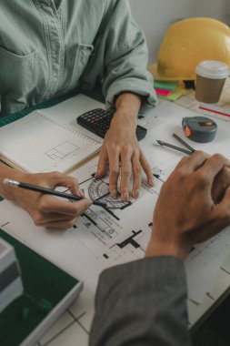 Mühendisler oturmuş yapıyı güçlendirmek için gözden geçirilmesi gereken bir inşaat planını tartışıyorlar. Bir mimar ve asistan planları inceliyor ve inceliyor.