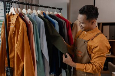 Bir tasarımcı atölyesinde çalışıyor, alışverişe gönderilmeden önce tüm kıyafetleri kontrol ediyor, yetenekli tasarımcı işinden memnun, şık. kumaş, dikiş, moda, girişimci