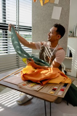 Moda tasarımcısı atölyesinde çalışıyor. Sevdiği şeyleri yapıyor. Bir elbise dikmek için dikiş makinesi kullanmak, elbiseyi dikmek için kumaşı seçmek gibi.