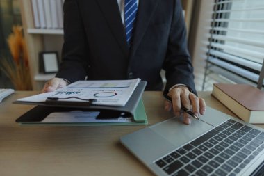 Bir işadamı elinde belgelerle bir ofiste oturmuş verileri analiz ediyor. Bir şirketin yöneticisi şirket sahibi olarak itibarını göstermek için takım elbise giyer..