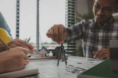 Mühendislerden oluşan bir ekip, tasarım yapısını analiz etmek ve müşterinin isteklerini karşılamak için ofiste toplanıyor. Mimarlar ve müteahhitlerden oluşan bir ekip, bir model eve dayanan tasarımı tartışmak için toplanıyor..