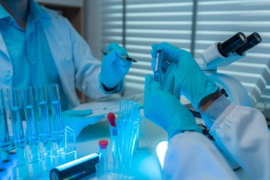 Bir bilim adamı ve asistanı laboratuarda mikroskop, test tüpü, deney tüpü, deney tüpü, pipet gibi birçok bilimsel ekipmanla birlikte çalışıyorlar.