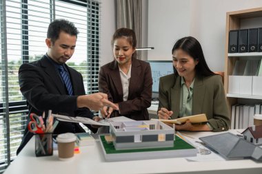 Mimarlar, ilk taslak planın doğruluğunu kontrol etmek için ofiste mühendis ve müteahhitlerle birlikte çalışırlar. Masanın üzerindeki plan, üç mimar iş yerinde birlikte çalışırlar.