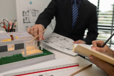 Mimarlar, ilk taslak planın doğruluğunu kontrol etmek için ofiste mühendis ve müteahhitlerle birlikte çalışırlar. Masanın üzerindeki plan, üç mimar iş yerinde birlikte çalışırlar.