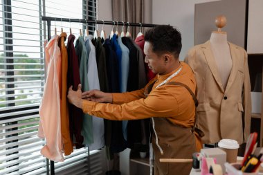 Bir tasarımcı atölyesinde çalışıyor, alışverişe gönderilmeden önce tüm kıyafetleri kontrol ediyor, yetenekli tasarımcı işinden memnun, şık. kumaş, dikiş, moda, girişimci