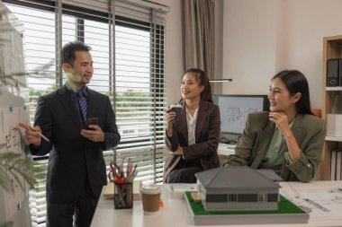 Mimarlar, ilk taslak planın doğruluğunu kontrol etmek için ofiste mühendis ve müteahhitlerle birlikte çalışırlar. Masanın üzerindeki plan, üç mimar iş yerinde birlikte çalışırlar.