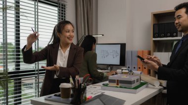 Ofiste bir mimar ekibiyle birlikte çalışıyor, planlar masanın üzerinde, müteahhit mühendislik ve mimari ile çalışıyor, ev modeli de masanın üstünde.