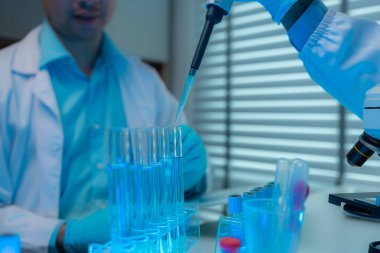 Bir bilim adamı ve asistanı laboratuarda mikroskop, test tüpü, deney tüpü, deney tüpü, pipet gibi birçok bilimsel ekipmanla birlikte çalışıyorlar.
