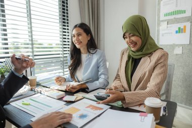 Bir grup iş adamı bir ofiste tartışıyorlar. Farklı kültürlerden iş adamları uygun ve dini açıdan doğru ürünler üretmek için toplanıyorlar. Bir iş kadını başörtüsü takıyor..