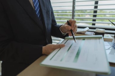 Bir işadamı elinde belgelerle bir ofiste oturmuş verileri analiz ediyor. Bir şirketin yöneticisi şirket sahibi olarak itibarını göstermek için takım elbise giyer..