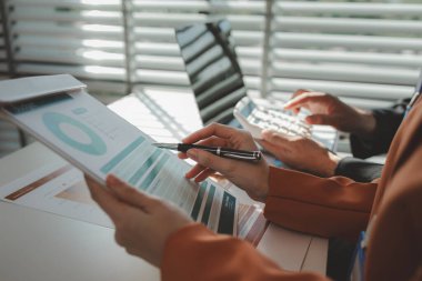 Gün boyunca bir ofiste çalışan bir çalışan masasında iş arkadaşlarıyla birlikte çalışıyor. Girişimciler şirketteki belgelerle çalışıyorlar.