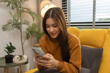 Gülümseyen genç bir kadın modern akıllı telefonu kullanıyor, çevrimiçi sohbet ediyor, evde dinlenen güzel bir kadın müzik dinliyor ve sevdiği diğer şeyler evde dinlenen düşünceli çok ırklı bir kadın.,