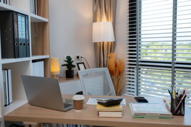 Açık dizüstü bilgisayarı, verimli çalışma ortamı, şık ahşap masası, modern ofis alanı ve profesyonel çalışma ortamı olan güneşli bir ofis masası..