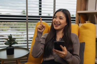 Gülümseyen genç bir kadın modern akıllı telefonu kullanıyor, çevrimiçi sohbet ediyor, evde dinlenen güzel bir kadın müzik dinliyor ve sevdiği diğer şeyler evde dinlenen düşünceli çok ırklı bir kadın.,