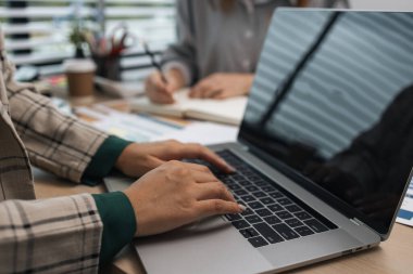 Bir iş kadını ekibine bilgi göndermek için elektronik bir cihaz kullanıyor. Pazarlama ekibi lideri, pazarlama verileriyle ilgili belgeleri inceliyor.