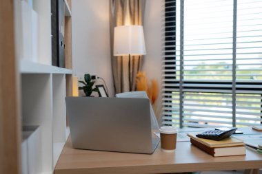 Açık dizüstü bilgisayarı, verimli çalışma ortamı, şık ahşap masası, modern ofis alanı ve profesyonel çalışma ortamı olan güneşli bir ofis masası..