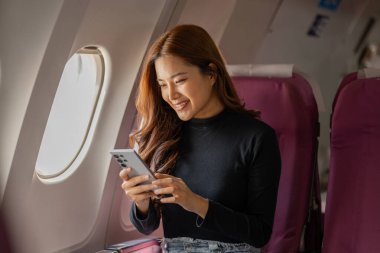 Genç, mutlu bir kadın bir uçak kabininde, güzel bir Asyalı kadın tatil için yabancı bir ülkeye uçakla gidiyor, uçağın içinde atmosfer, uçakta çeşitli pozlar veren bir kadın..