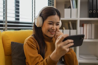 Gülümseyen genç bir kadın modern akıllı telefonu kullanıyor, çevrimiçi sohbet ediyor, evde dinlenen güzel bir kadın müzik dinliyor ve sevdiği diğer şeyler evde dinlenen düşünceli çok ırklı bir kadın.,