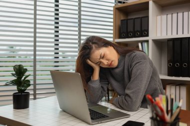 Ofisinde dizüstü bilgisayarı olan yorgun genç bir kadın, iş kadını, son teslim tarihi için ofiste stres, beyin sisi ve fazla mesai, yorgunluk ve yönetim için bunalmış
