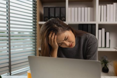 Ofisinde dizüstü bilgisayarı olan yorgun genç bir kadın, iş kadını, son teslim tarihi için ofiste stres, beyin sisi ve fazla mesai, yorgunluk ve yönetim için bunalmış