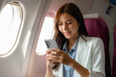 Asyalı bir kadın uçakla yurtdışına seyahat ediyor. Kadın gezgin kendini eğlendirmek için elektronik cihazını kullanıyor. Yurtdışında uçan genç bir kadın, yolcu, uçuş...