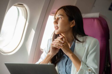 Asyalı bir kadın uçakla yurtdışına seyahat ediyor. Kadın gezgin kendini eğlendirmek için elektronik cihazını kullanıyor. Yurtdışında uçan genç bir kadın, yolcu, uçuş...