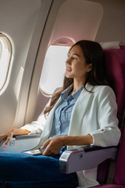 Asyalı bir kadın uçakla yurtdışına seyahat ediyor. Kadın gezgin kendini eğlendirmek için elektronik cihazını kullanıyor. Yurtdışında uçan genç bir kadın, yolcu, uçuş...