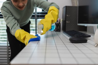 Şirketin temizlikçisi, yöneticinin ofisini özenle temizlerken temizlikçi kadın, tahriş edici kimyasalları temizlerken lastik eldiven giyer.