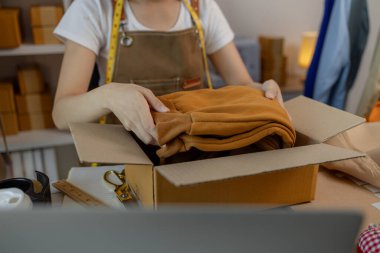 Güzel bir kadın giyim mağazası sahibi müşterilerle sohbet etmek için canlı yayın yapıyor ve ürünlerini müşterilere, paketlere, terzilere, tasarımcılara nakliyeye hazırlanmak için doxlara dolduruyor.