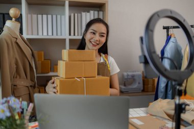Güzel bir kadın giyim mağazası sahibi müşterilerle sohbet etmek için canlı yayın yapıyor ve ürünlerini müşterilere, paketlere, terzilere, tasarımcılara nakliyeye hazırlanmak için doxlara dolduruyor.
