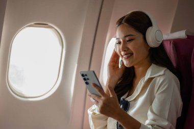 Asyalı bir kadın uçakla yurtdışına seyahat ediyor. Kadın gezgin kendini eğlendirmek için elektronik cihazını kullanıyor. Yurtdışında uçan genç bir kadın, yolcu, uçuş...