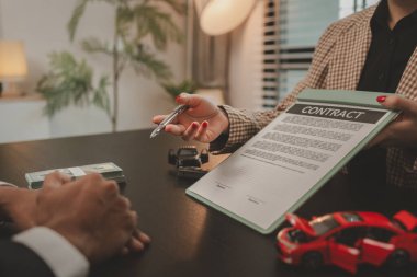 Bir araba satıcısı, satış sözleşmesini imzalamadan önce araba satın alma sözleşmesinin detaylarını müşteriye açıklar. Galeri, satıcı, araba sözleşmesi, araba satın alma sözleşmesi.