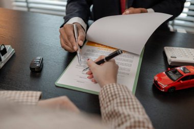 Bir araba satıcısı, satış sözleşmesini imzalamadan önce araba satın alma sözleşmesinin detaylarını müşteriye açıklar. Galeri, satıcı, araba sözleşmesi, araba satın alma sözleşmesi.