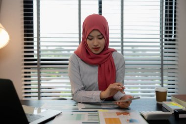 Müslüman bir kadın çalışan, özel ofisindeki bir şirkette mali ve muhasebe belgeleri üzerinde çalışıyor, tesettür, pazarlama, kadın müslüman şirket başkanı ofisinde çalışıyor.