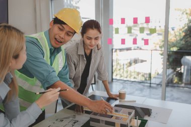 Mimar ve ekibi, bina modeli, mühendis ve takım çalışması ile planlardaki yapısal planların nasıl kontrol edileceği konusunda beyin fırtınası yapmak için inşaat yöneticisiyle görüşüyor.