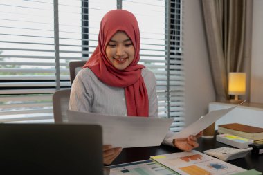 Müslüman bir kadın çalışan, özel ofisindeki bir şirkette mali ve muhasebe belgeleri üzerinde çalışıyor, tesettür, pazarlama, kadın müslüman şirket başkanı ofisinde çalışıyor.