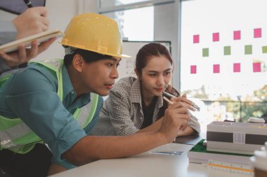 Mimar ve ekibi, bina modeli, mühendis ve takım çalışması ile planlardaki yapısal planların nasıl kontrol edileceği konusunda beyin fırtınası yapmak için inşaat yöneticisiyle görüşüyor.