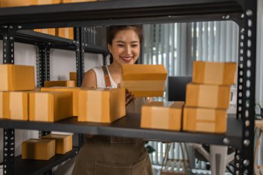 Paketleyici, bir müşteriye teslim edilmeden önce paketin durumunu kontrol eder, küçük bir işletme sahibi bir depodaki kutuları inceler, raflarla dolu bir depo ve paket
