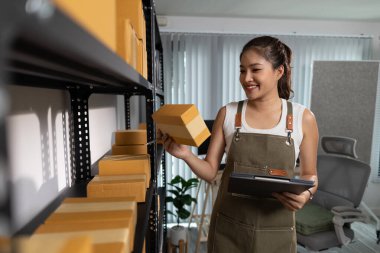 Bir bayan çalışan depodaki paket kutularını kontrol ediyor, bir depo müdürü raflardaki paket kutularını sayıyor, küçük bir online işletme sahibi bir depo odasında.