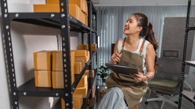 Bir bayan çalışan depodaki paket kutularını kontrol ediyor, bir depo müdürü raflardaki paket kutularını sayıyor, küçük bir online işletme sahibi bir depo odasında.