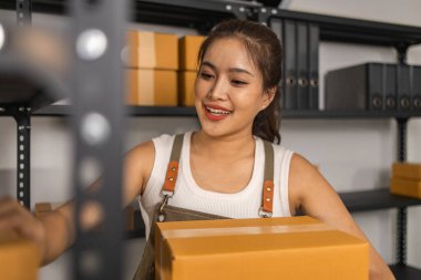 Paketleyici, bir müşteriye teslim edilmeden önce paketin durumunu kontrol eder, küçük bir işletme sahibi bir depodaki kutuları inceler, raflarla dolu bir depo ve paket