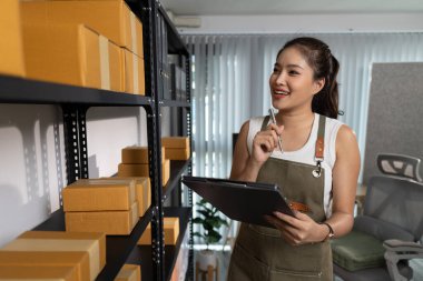 Paketleyici, bir müşteriye teslim edilmeden önce paketin durumunu kontrol eder, küçük bir işletme sahibi bir depodaki kutuları inceler, raflarla dolu bir depo ve paket